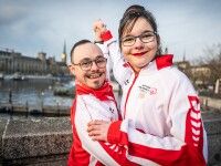 One man and one woman wearing Special Olympics Switzerland gear dancing and smiling at the camera on a bridge 