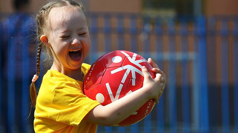 Young girl holding Special Olympics soccer ball, smiling and laughing. 