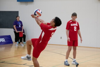 Male athlete hitting the ball while his teammate and official watch. 