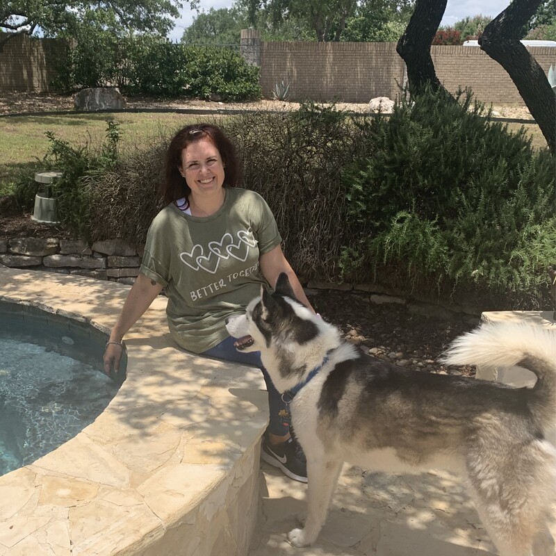 Ashley Muth in a green "Better Together" t-shirt sitting down with her dog.