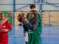 A female basketball player attempts a shot, while another player tries to block her, and a third player watches from the background.