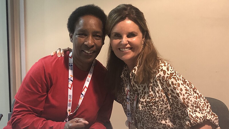 Loretta Claiborne and Maria Shriver sitting down both smiling; Maria has her arm around Loretta's shoulder.