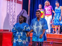 Participants walk hand-in-hand down a stage runway during an inclusive fashion show, wearing coordinated blue patterned outfits.