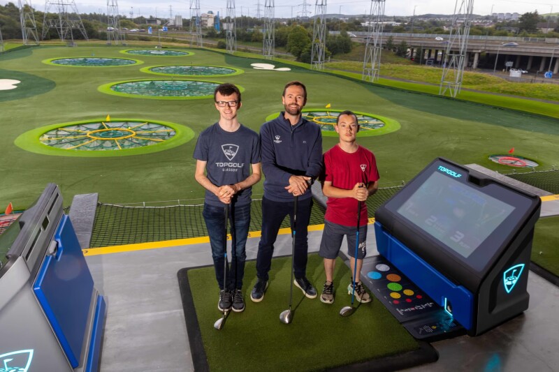 Three people standing on a platform at Topgolf