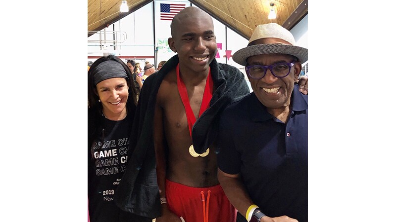 Young man (Nick) his father (Al Roker) and a woman stand together side by side; Nick has two gold metals around his neck. 