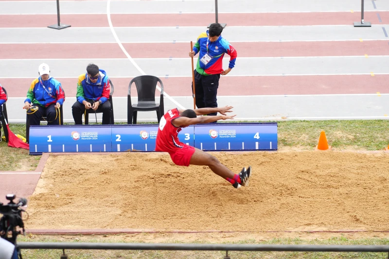 Atleta realizando un salto de longitud durante una competición, demostrando esfuerzo, superación y determinación en un evento de Olimpiadas Especiales.