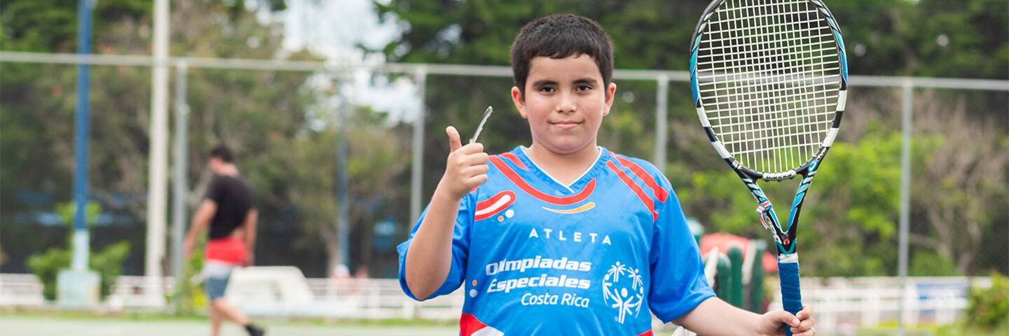 AJ (from Costa Rica) on the tennis court giving a thumbs up and holding a tennis racket.