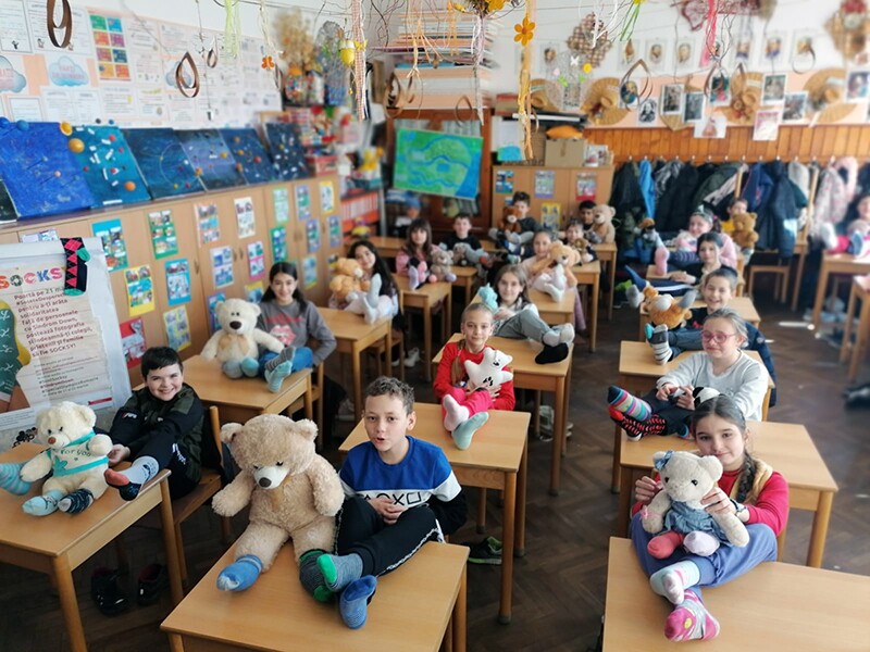 A group of young children in class sitting at their desks with teddy bears on their desks. 