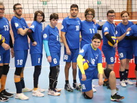 A group of volleyball players stand together as a team wearing blue kits in front of a volleyball net. 