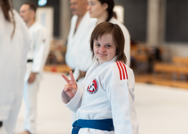 A young woman wearing a judogi and making a peace sign