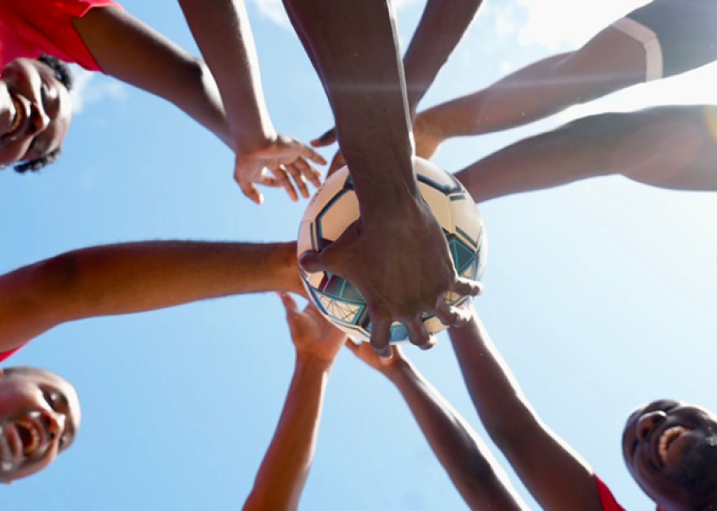 a group of athletes standing in a circle putting their hands in the middle, one on top of the other. 