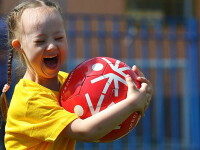 Young girl holding Special Olympics soccer ball, smiling and laughing. 