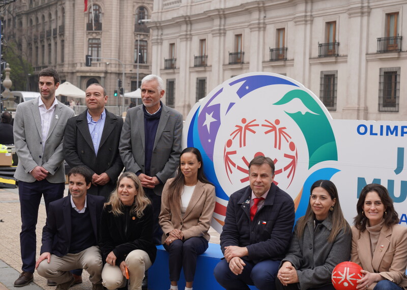 A group of 10 people in two rows in front of Santiago 2027 branded signage. 