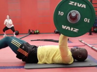 Banele laying on the ground in a gym doing chest presses. 