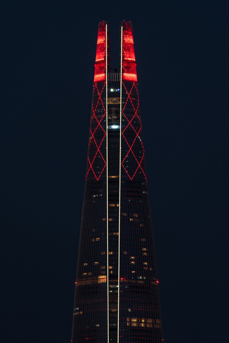 Jamsil Lotte World Tower, the tallest building in Korea, lit up red at the top, the night dark night sky is in the background.