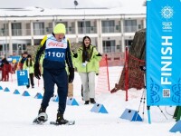 A man wearing snowshoes competes in a snowshoeing competition as fans and spectators watch. A white building is pictured in the background