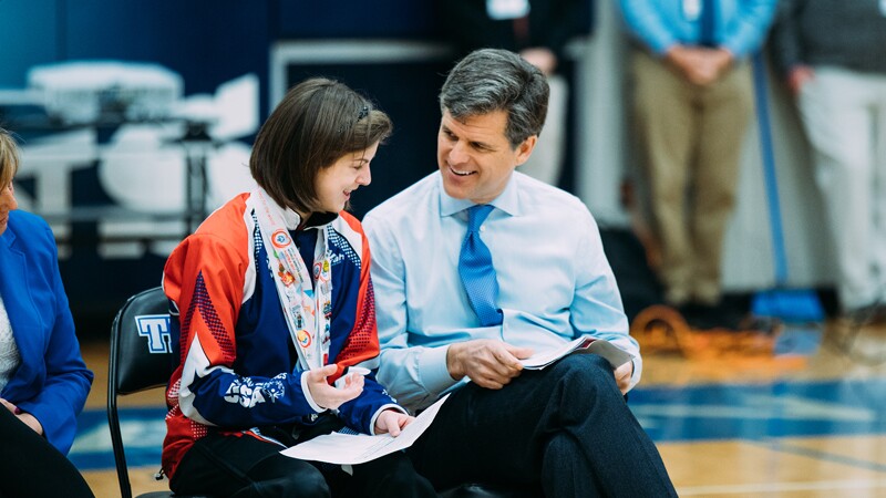 Tim Shriver sits next to female student at a high school assembly.