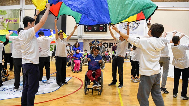 Young adults and athletes playing parachute in a gymnasium.
