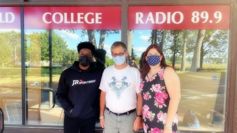 Three people—two men on the left and one woman on the right—standing in front of a store front. 