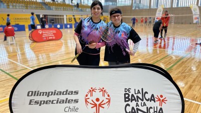 two girls pose with badminton rackets in front of Special Olympics Chile Unified Schools’ sign