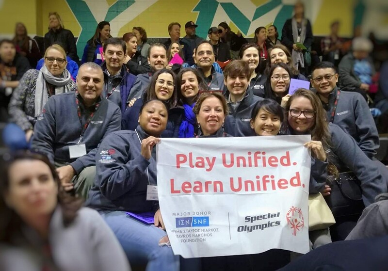 Special Olympics staff and representatives at a Play unified Learn Unified event sitting in a group holding up a banner. 