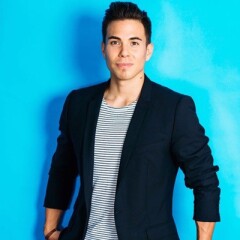 Apolo Ohno's standing in front of a light blue wall in a black jacket and white and black striped shirt