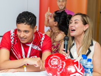 A man and woman at a table, the women is speaking into a microphone. 