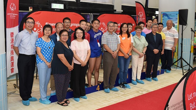 Participants, athletes, parents and representatives of the 42nd Special Olympics Hong Kong Swimming Competition stand in a row shoulder to shoulder in front of Special Olympics signage.