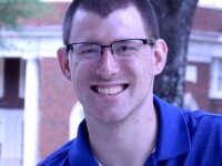 RJ smiling for a photo; he has on glasses and a blue polo. 