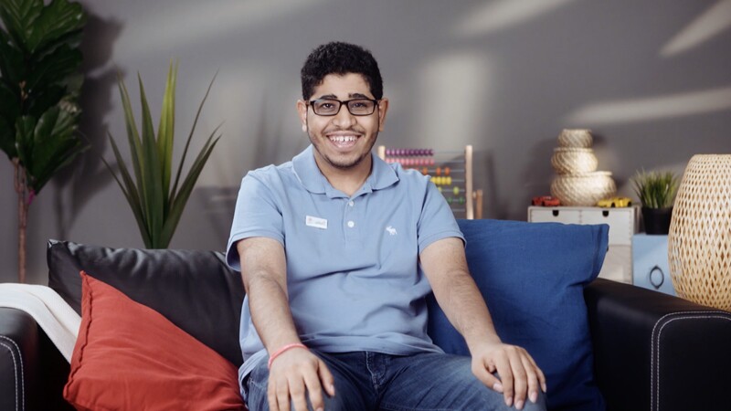 Ahmad sitting on a couch in a blue polo shirt smiling for the photo.