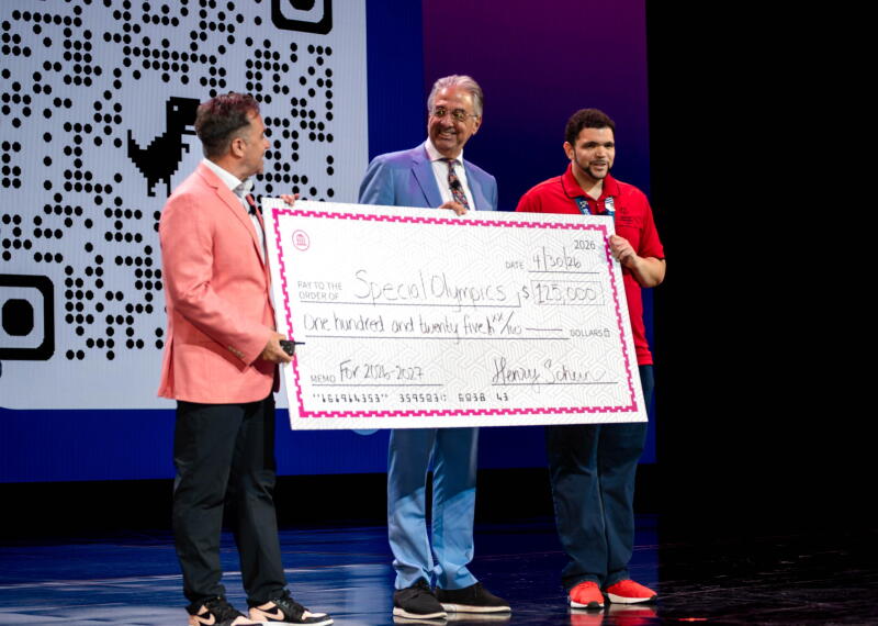 Three people holding a large-sized check while standing on a stage.