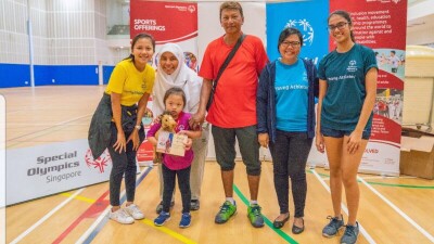 Hadbaa at a young age stands in front of Special Olympics Singapore signs with her family.