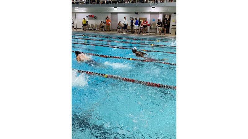 Athletes swimming in a pool during a race; onlooker watch the action. 