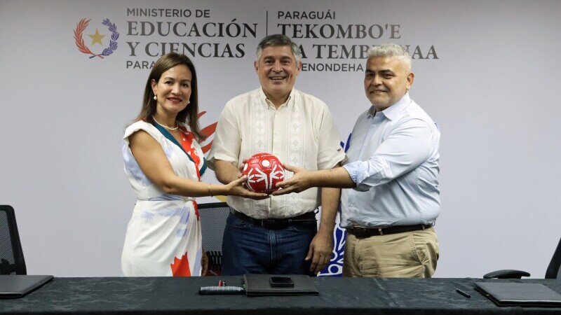 A woman and two men smile while holding a soccer ball bearing the Special Olympics logo