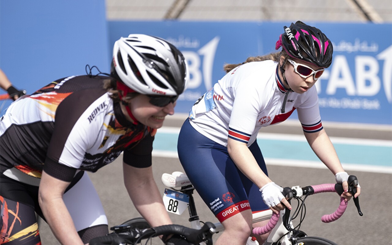 Kiera riding her bike next to another athlete. Both have safety helmets on.
