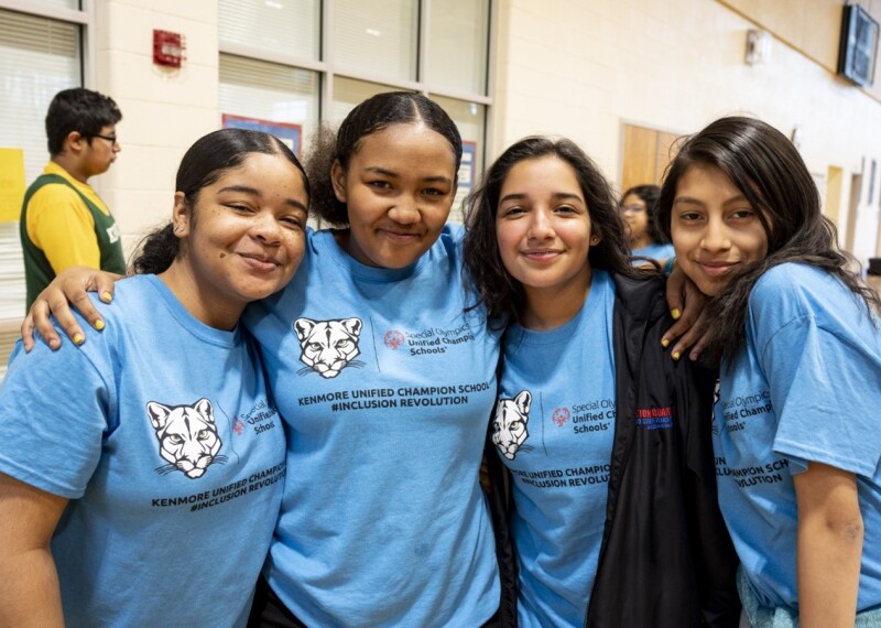 Four girls with their arms around one another's shoulders. 