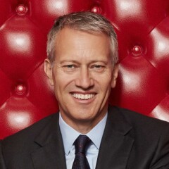 Professional photo of James Quincey sitting on a red high-backed couch.