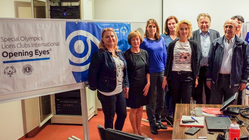 A group of eye specialists stand together beside an Opening Eyes banner and eye equipment.