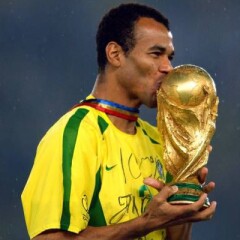 Cafu wearing his yellow and green jersey with a blue gold and red ribbon around his neck holding and kissing a gold trophy
