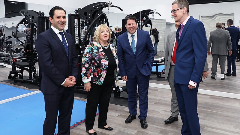 A group of adults dressed up standing in a gymnasium opening and talking.