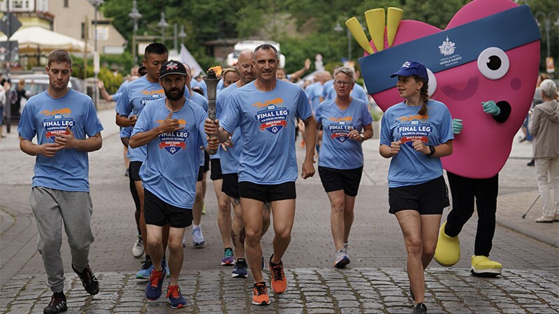 The pick heart shaped logo jogs alongside approximately six runners.