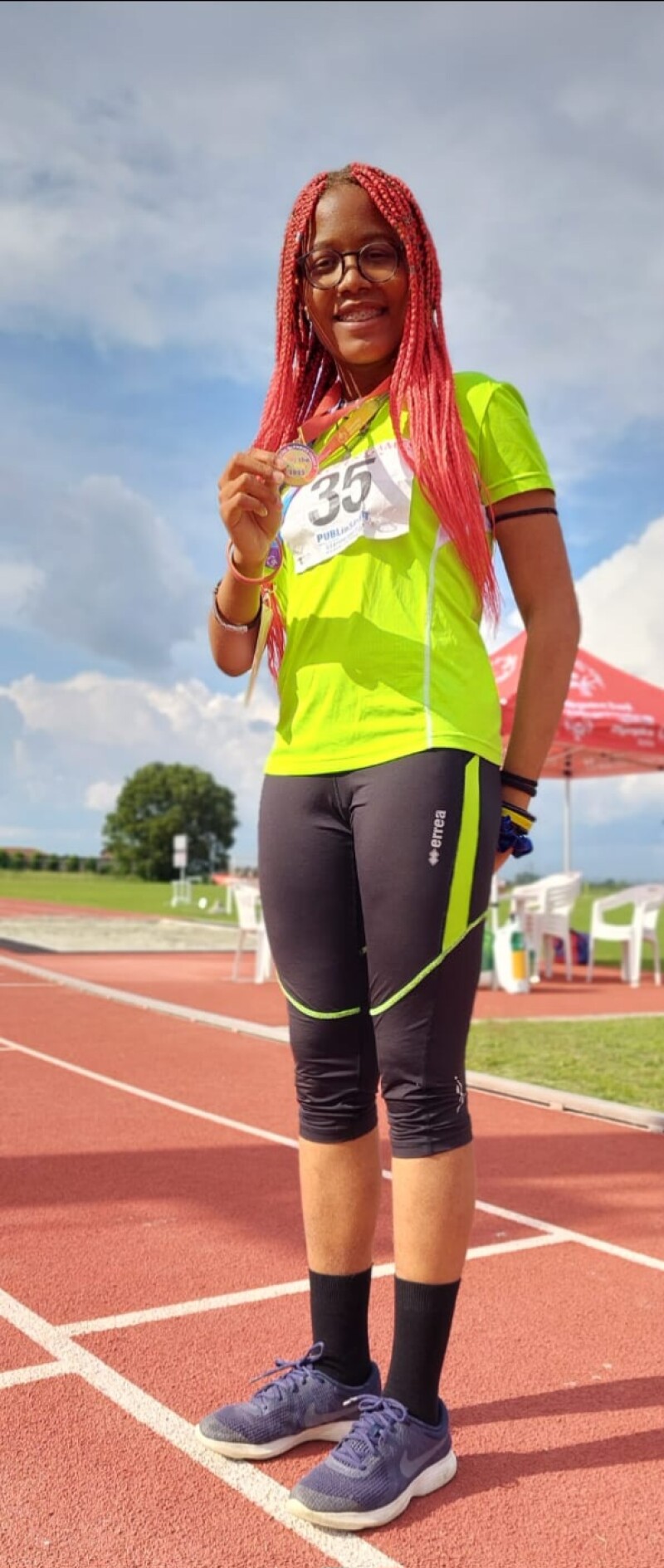 Athlete posing for the camera while holding a medal and standing on the track