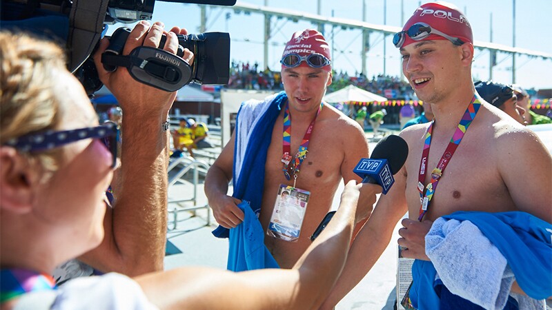 Two swimmers—post race—being interviewed by the press by the swimming pool.