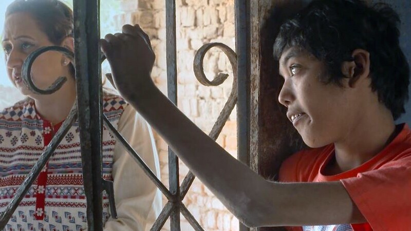 Young man holding onto a decorative iron bar and looking off into the distance. 