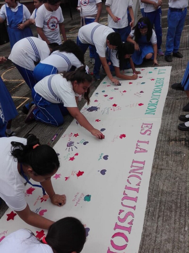 A group of students and athletes sign and decorate an inclusion banner outside.