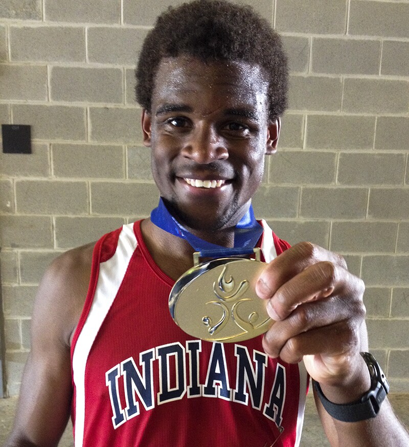 Athlete in a red tank top that reads, Indiana showing off his gold medal.