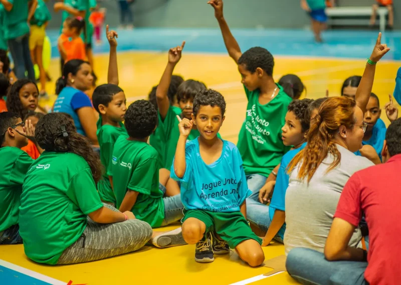 Un grupo de niños participa en una actividad deportiva inclusiva en una cancha. Varios levantan la mano mientras esperan instrucciones.