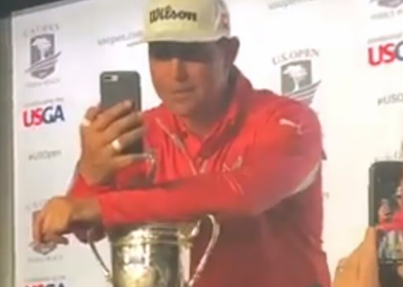 PGA Golf Player on stage looking at his mobile phone and talking to an athlete. Audience member can be seen making a video. 