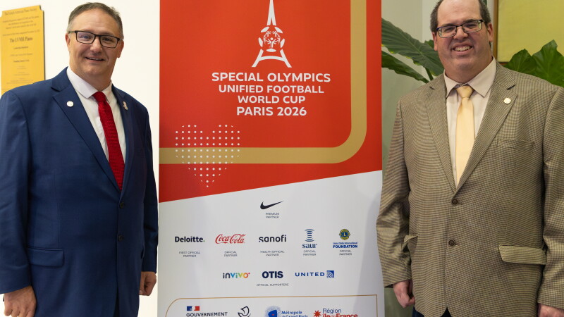 Two men standing on either side of Special Olympics Unified Football World Cup 2026 signage. 