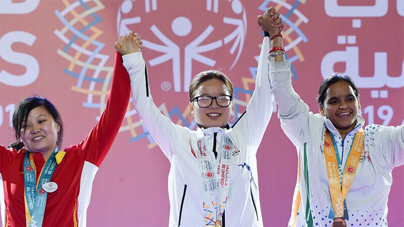 Three athletes at a medaling ceremony holding hands up in the air as a sign of victory.
